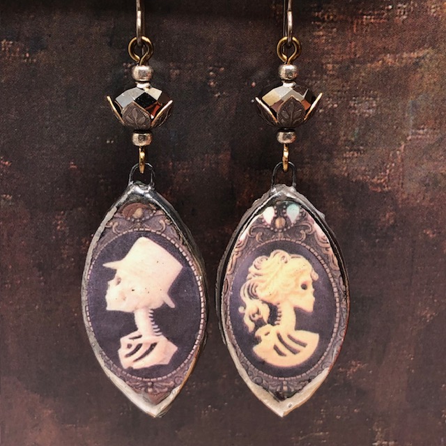 Boucles d'oreilles asymétriques ovales composées de pendentifs en céramique représentant un couple de squelettes blancs sur un fond noir. Bijoux uniques.