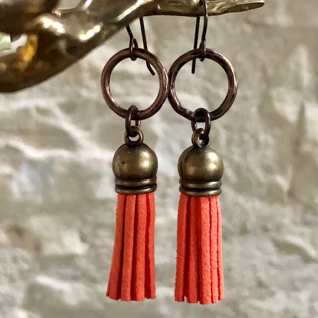 Boucles d’oreilles composées de pompons en suédine orange et surmontées d’anneaux en laiton. Crochets d'oreilles en laiton.