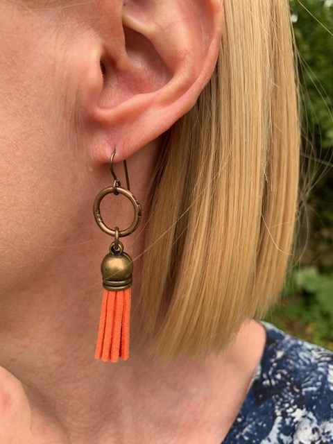 Boucles d’oreilles composées de pompons en suédine orange et surmontées d’anneaux en laiton. Crochets d'oreilles en laiton.