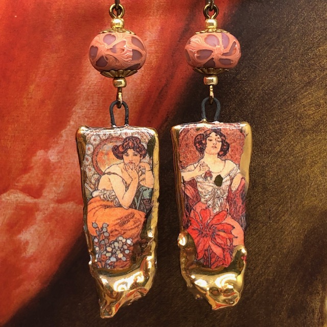 Boucles d’oreilles composées de pendentifs artisanaux en céramique représentant deux tableaux de Mucha intitulés Topaze et Rubis. Pièces uniques.