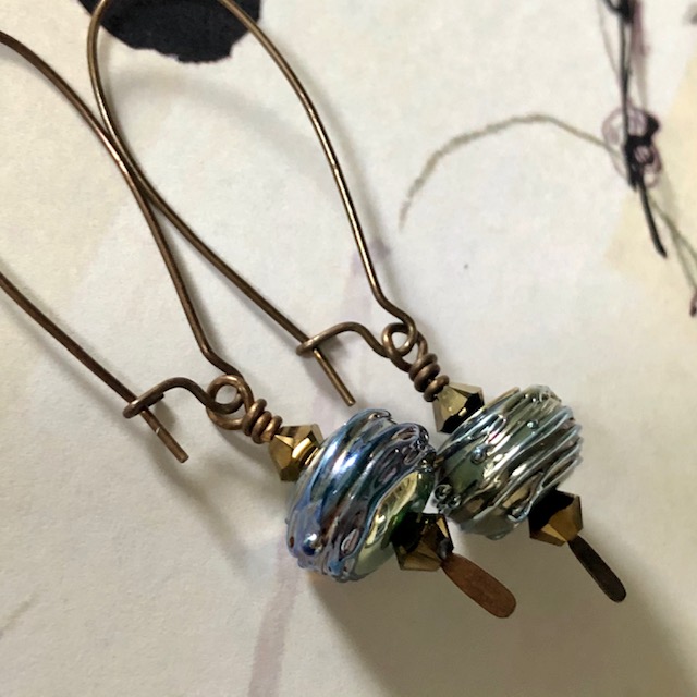 Boucles d'oreilles composées de  perles artisanales en verre filé au chalumeau bleu-verre et de perles en cristal Swarovski. Crochets d'oreilles en laiton.