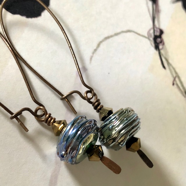Boucles d'oreilles composées de  perles artisanales en verre filé au chalumeau bleu-verre et de perles en cristal Swarovski. Crochets d'oreilles en laiton.