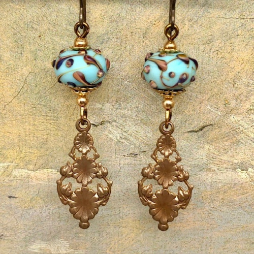 Boucles d'oreilles vintage composées de perles en verre filé à la flamme bleu turquoise et bronze et de pendentifs floraux en laiton. Bijoux uniques.