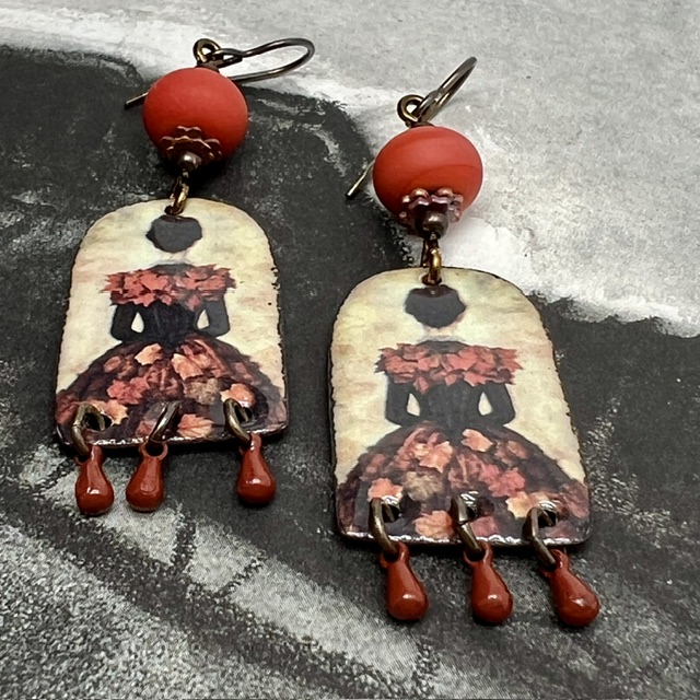 Boucles d’oreilles poétiques et composées de pendentifs en cuivre émaillé avec le portrait d'une femme vêtue d'une robe noire ornée de feuilles d'automne.