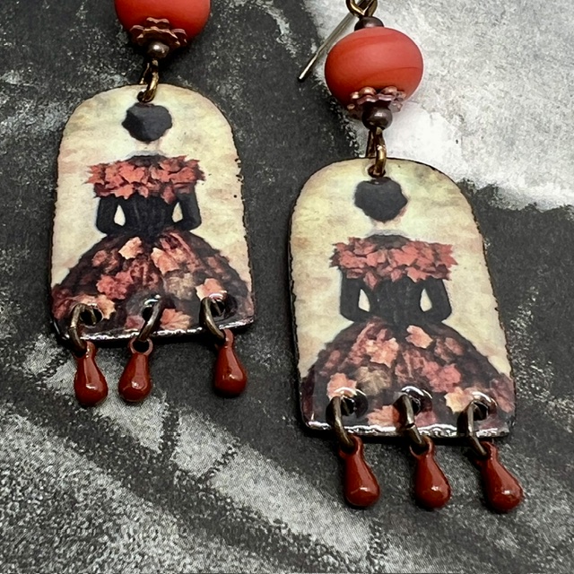 Boucles d’oreilles poétiques et composées de pendentifs en cuivre émaillé avec le portrait d'une femme vêtue d'une robe noire ornée de feuilles d'automne.