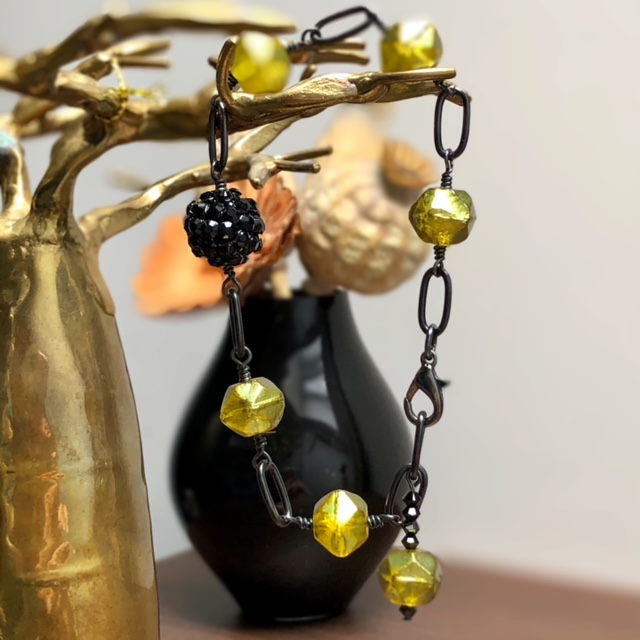 Bracelet composé de perles en verre tchèque et d'une perle noire en plasticine ornée de strass. Chaîne et fermoir en laiton. Pièce unique.