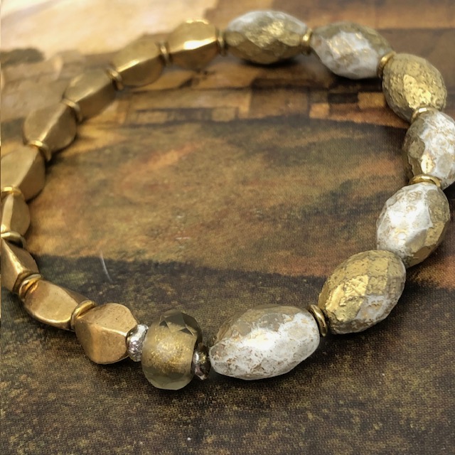 Bracelet élastique bohème chic composé de perles en verre de Bohême ovales, doré et blanche et de perles africaines en laiton doré.