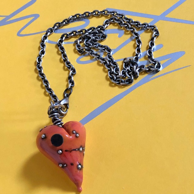Collier composé d'un pendentif artisanal en céramique en forme de coeur. Ce coeur clouté est suspendu à une chaîne en argent massif. Pièce unique.