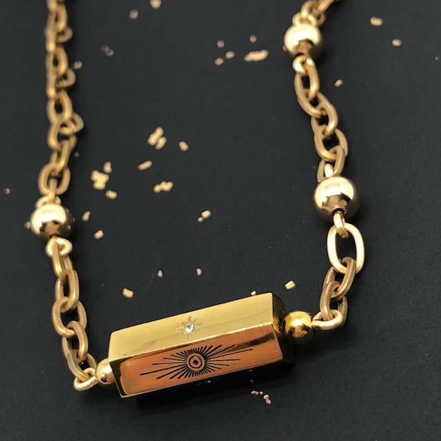Collier bohème chic composé d'une chaîne en laiton dorée, d'une perle cylindre en acier inoxydable doré avec un motif soleil et étoile du Nord.