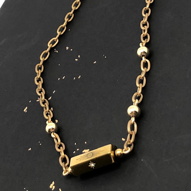 Collier bohème chic composé d'une chaîne en laiton dorée, d'une perle cylindre en acier inoxydable doré avec un motif soleil et étoile du Nord.