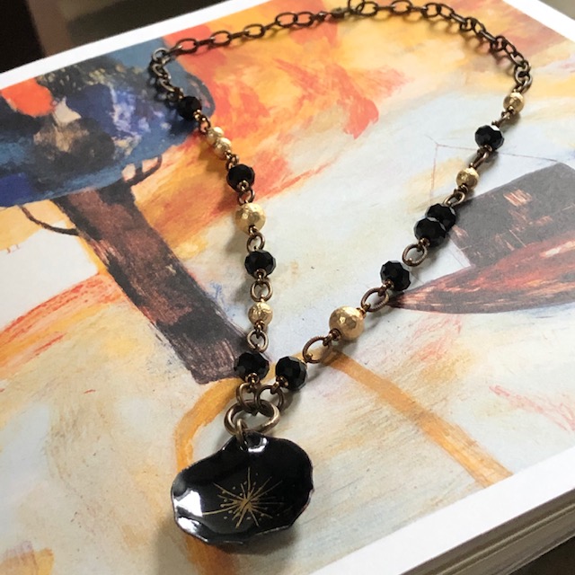 Collier bohème composé d'un pendentif en émail qui représente une fleur noire et or, de perles noires en cristal Swarovski et de perles en laiton doré.