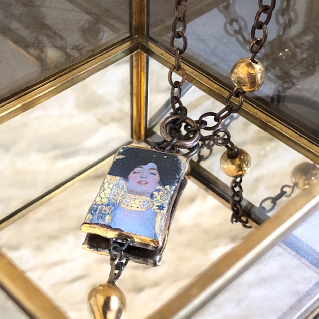 Collier composé d'un pendentif artisanal en céramique représentant Judith de Klimt et de perles dorées en céramique. Chaîne en laiton. Pièce unique.