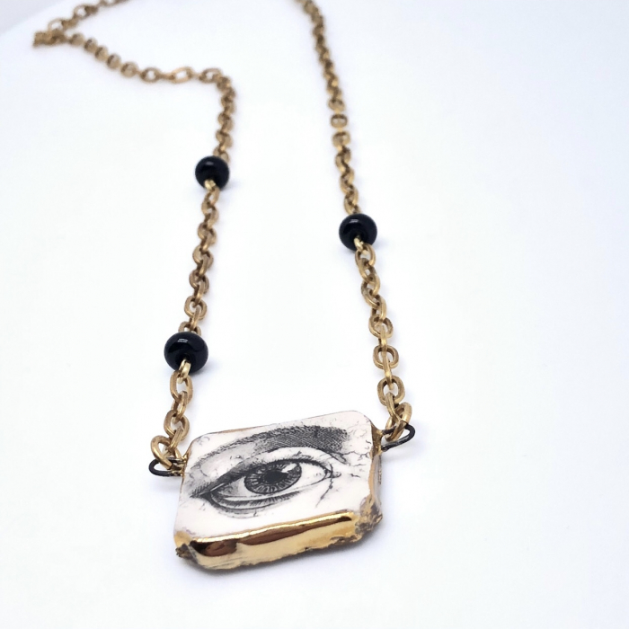 Sautoir composé d'un pendentif artisanal en céramique, de perles en verre filé au chalumeau noires et d'une chaîne artisanale en laiton doré. Pièce unique.